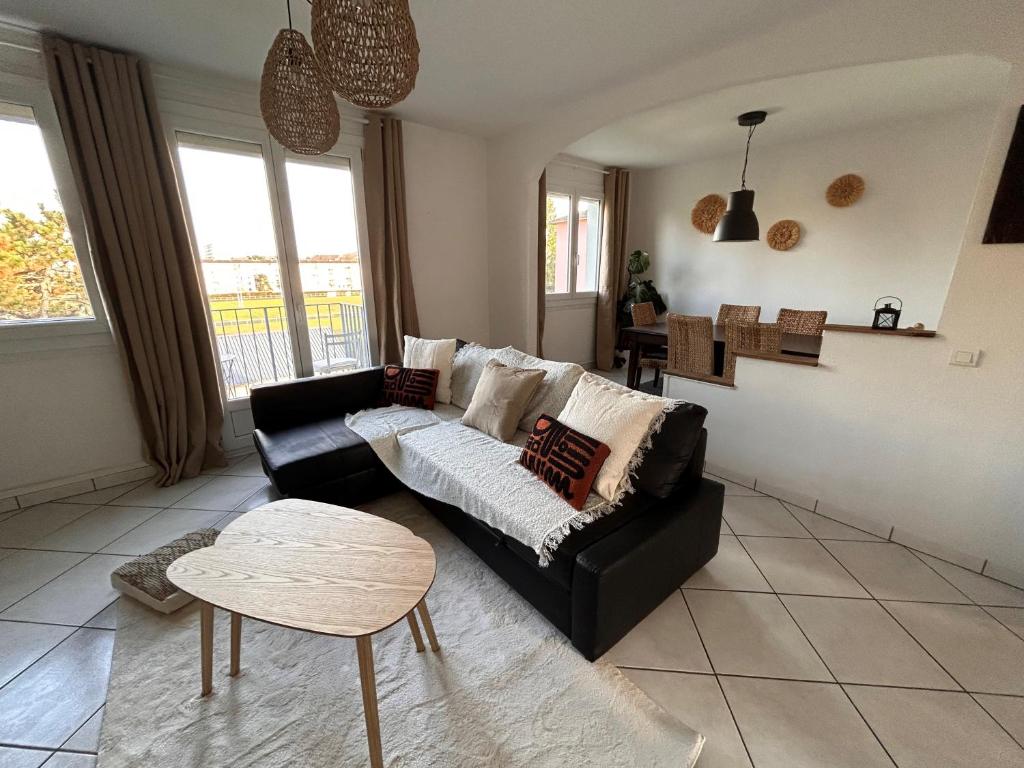 ein Wohnzimmer mit einem schwarzen Sofa und einem Tisch in der Unterkunft LA BELLE ESCALE in Belfort