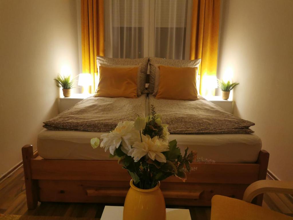 1 dormitorio con 1 cama con un jarrón de flores sobre una mesa en Római 1, en Dunaújváros