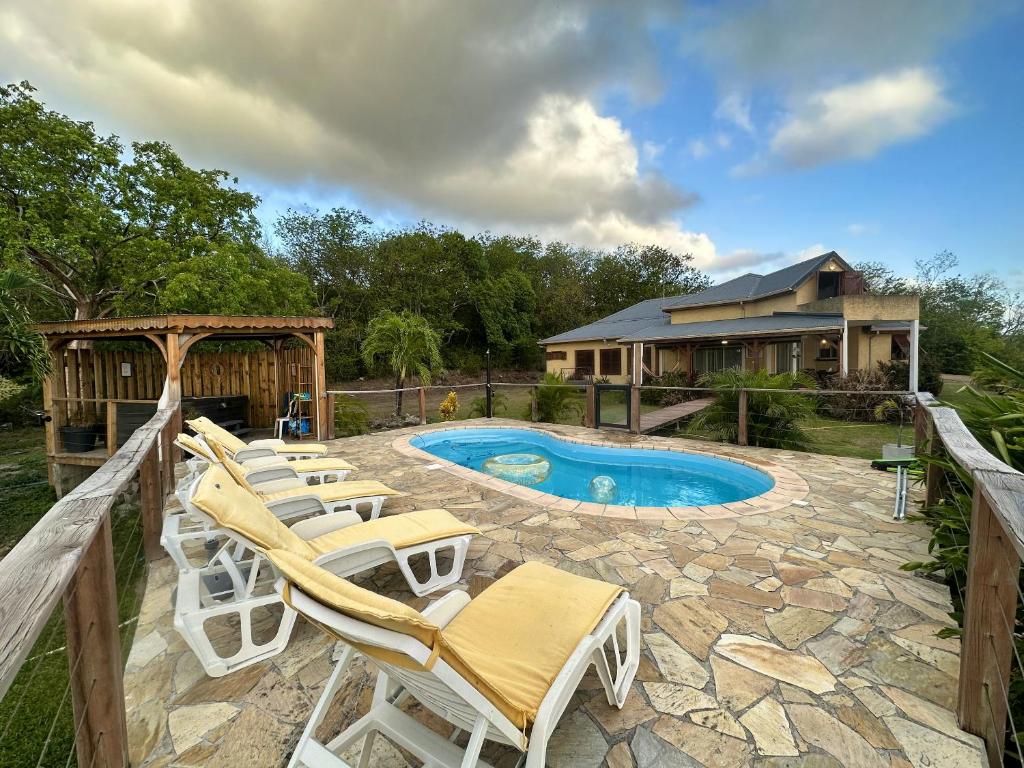 a backyard with a pool and chairs and a house at Maison conviviale à Deshaies avec piscine partagée 120 m² in Deshaies