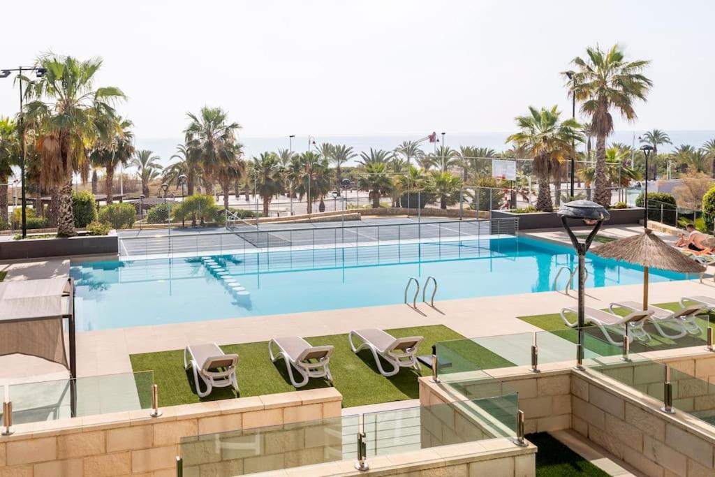 a large swimming pool with chairs and palm trees at Relax, vacaciones y lujo a 15 metros del mar in Arenales del Sol