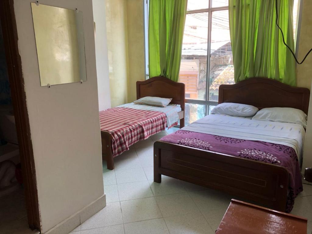 a room with two beds and a window with green curtains at Hotel SION in Pitalito