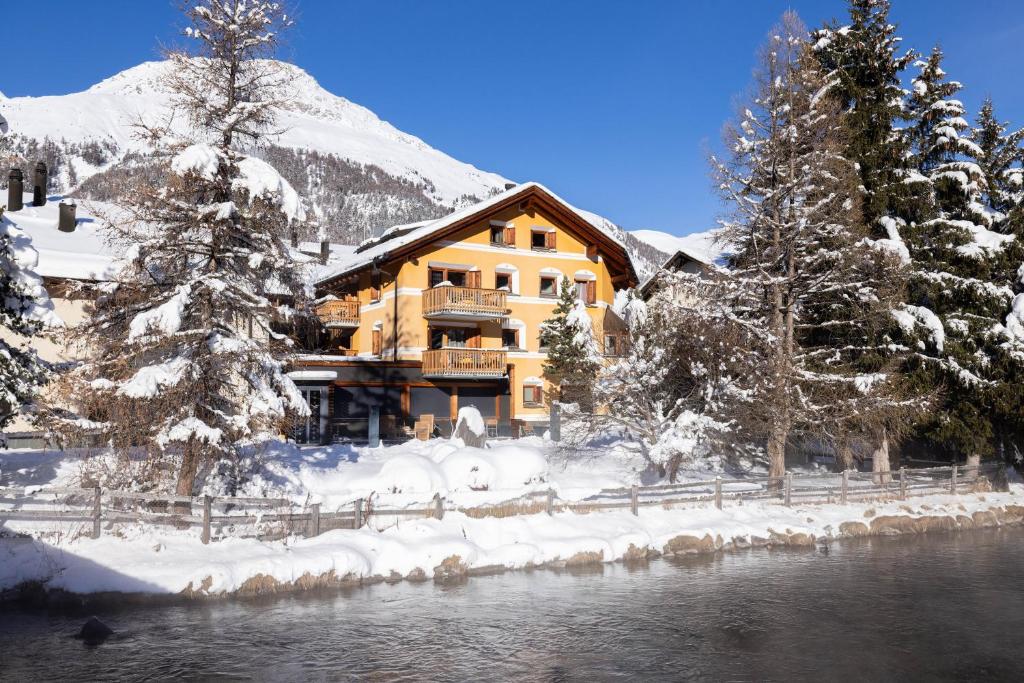 a house in the snow next to a river at Hotel Chesa Rosatsch - Home of Food in Celerina