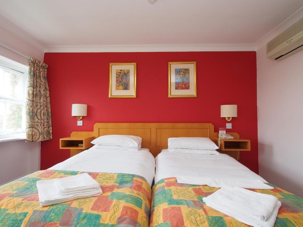 two beds in a room with a red wall at The Chatsworth Hotel in Worthing