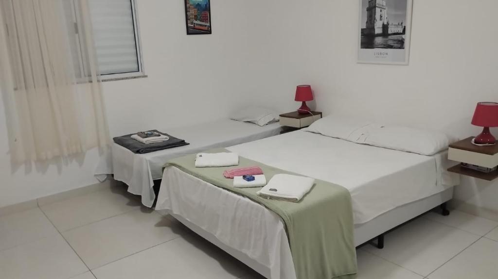 two beds in a white room with a table and two at Loft LISBOA para Casais, em Iguaba Grande, 3 Pessoas, 150 metros da praia in Iguaba Grande