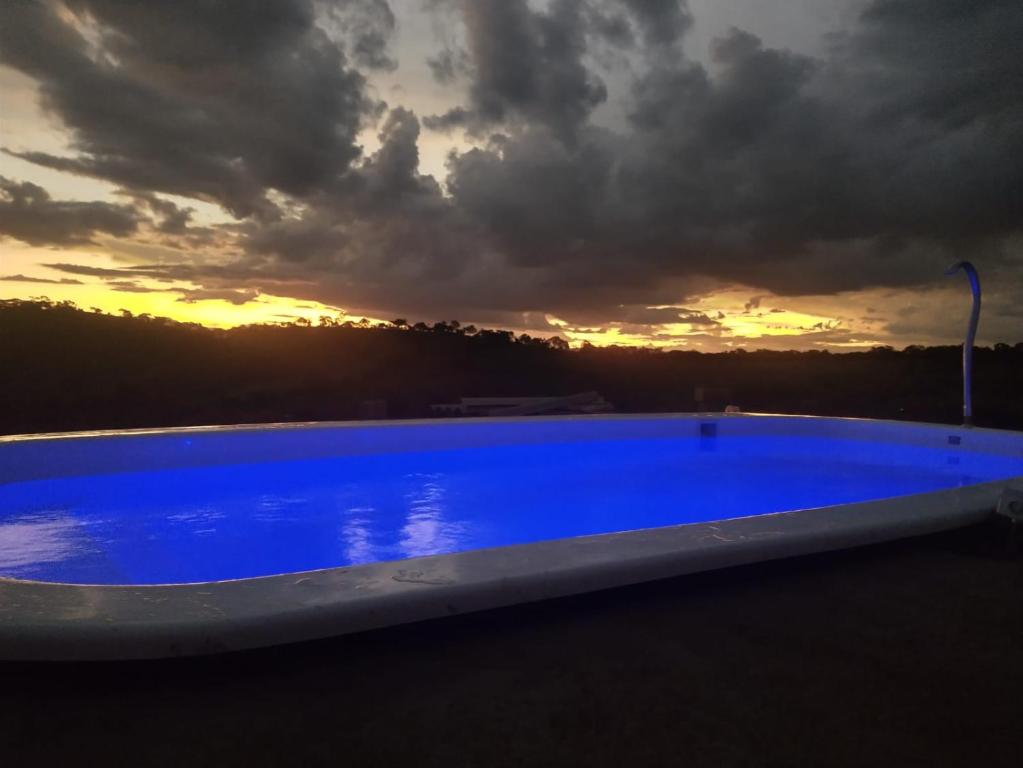 una piscina azul con puesta de sol en el fondo en Chácara Paraíso, en Pouso Alto