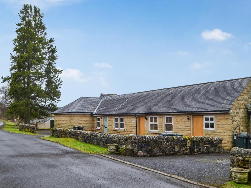 a house with a stone wall next to a street at The Waiting Room in Falstone