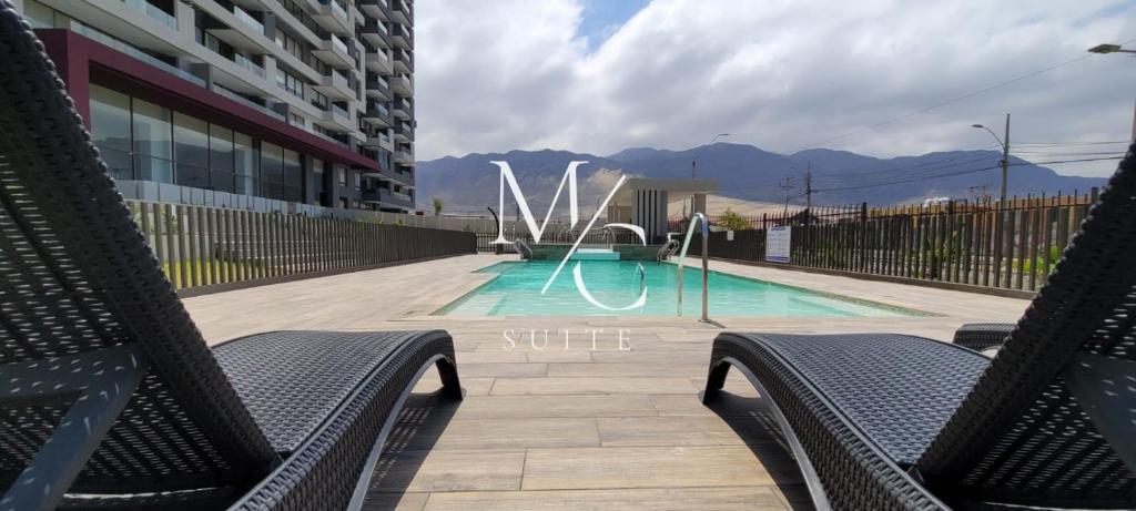 a swimming pool with two chairs in front of a building at MC Suite Norte in Antofagasta