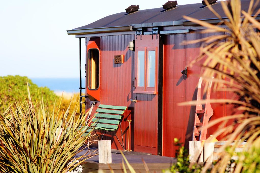 a small red house with a red door and some plants at Hapuku Carriages Kaikōura in Kaikoura