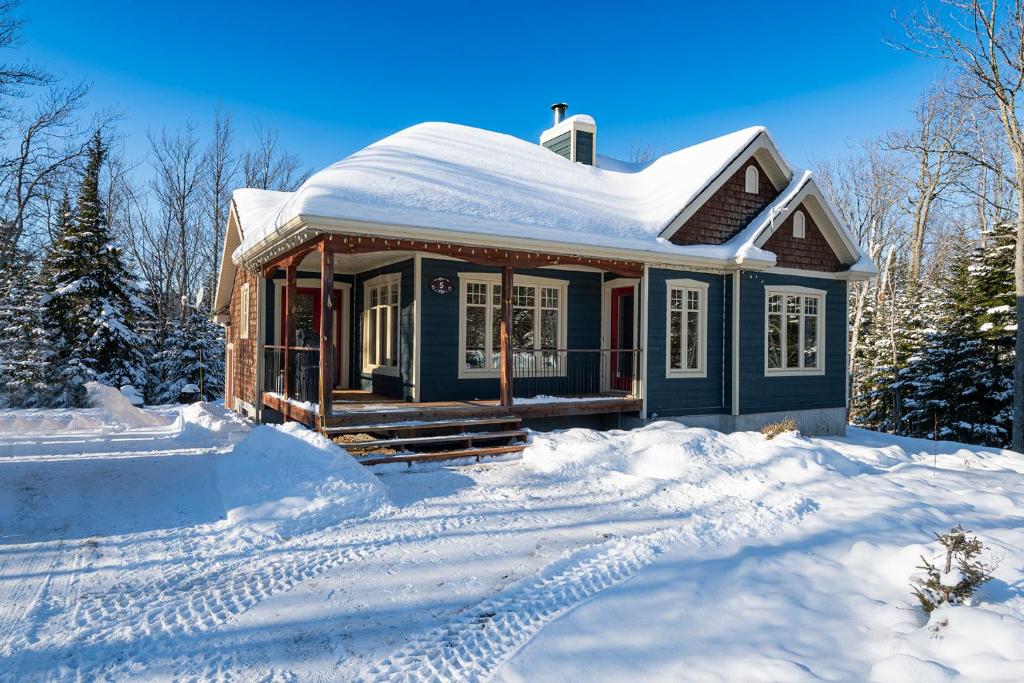 une petite maison bleue avec de la neige au sol dans l'établissement Chalet le Boréal: Massif, spa et montagnes, à Petite-Rivière-Saint-François