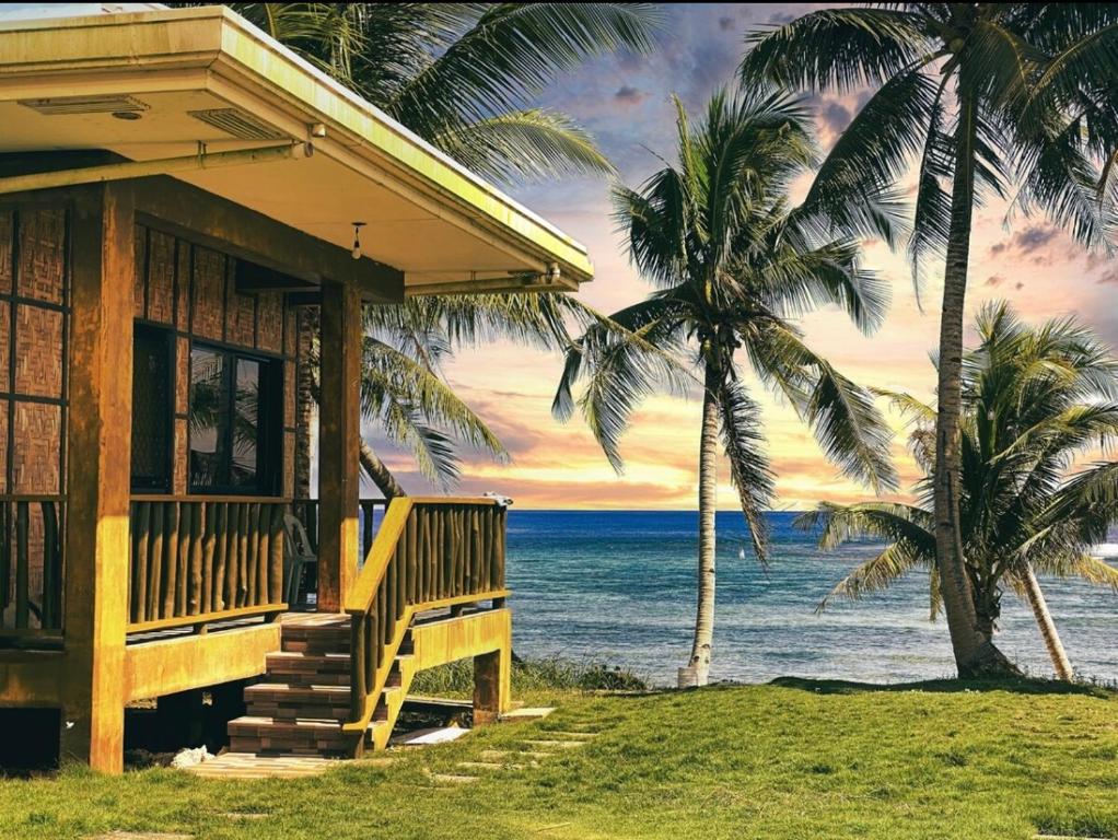 a house on the beach with two palm trees at Villa Malinao Oceanview Resort- Superior Bungalow in Burgos