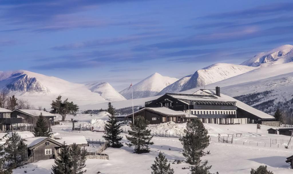 een gebouw in de sneeuw met bergen op de achtergrond bij Rondablikk Fjellstasjon in Mysusæter
