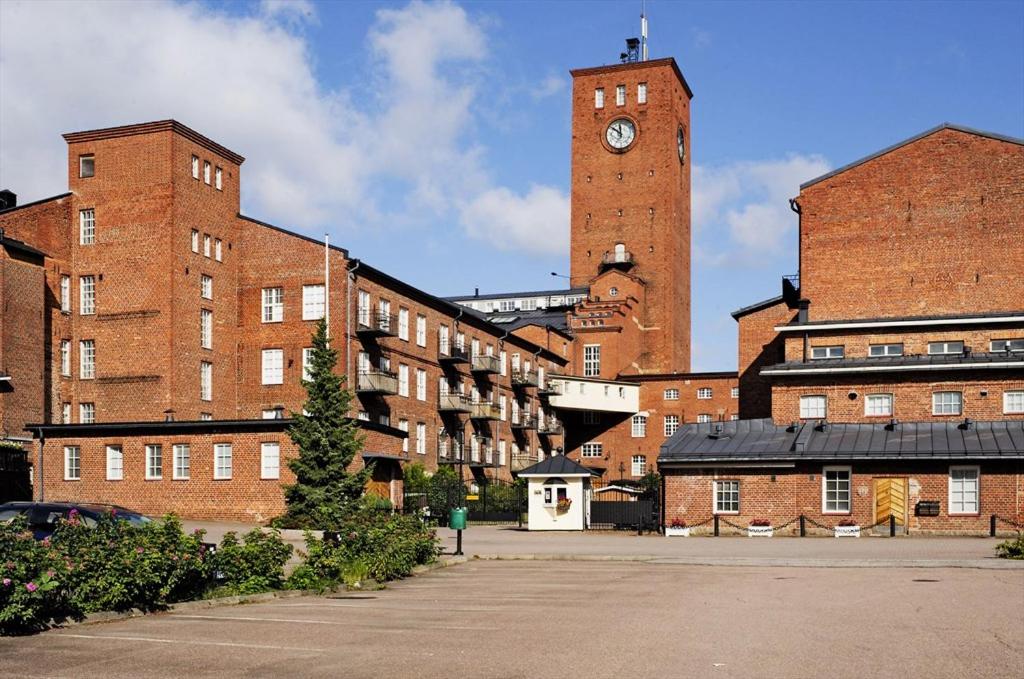 a group of brick buildings with a clock tower at Ilmastoitu yksiö Turun kupeessa in Lieto