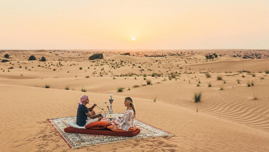 un hombre y una mujer sentados en una manta en el desierto en Luxury The Sunrise Resort with swimming pool Jaisalmer, en Jaisalmer