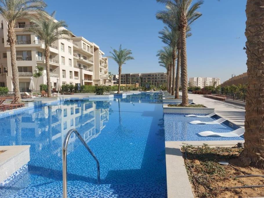 a swimming pool with palm trees and a building at Alumia Marigold Suite 3BR Apt Pool Access in Cairo