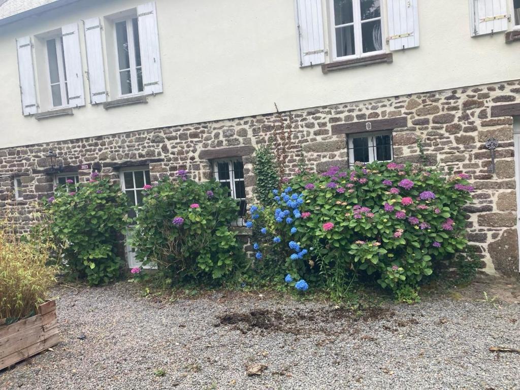 a stone house with flowers in front of it at Maison d'hôtes Petit Coin de Paradis in Moyon