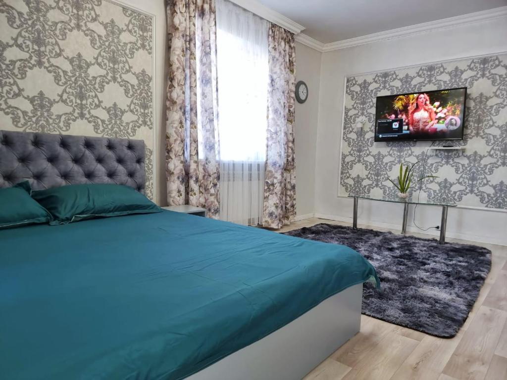 een slaapkamer met een bed en een tv aan de muur bij Уютная квартира в хорошем районе Тауке хана in Simkent
