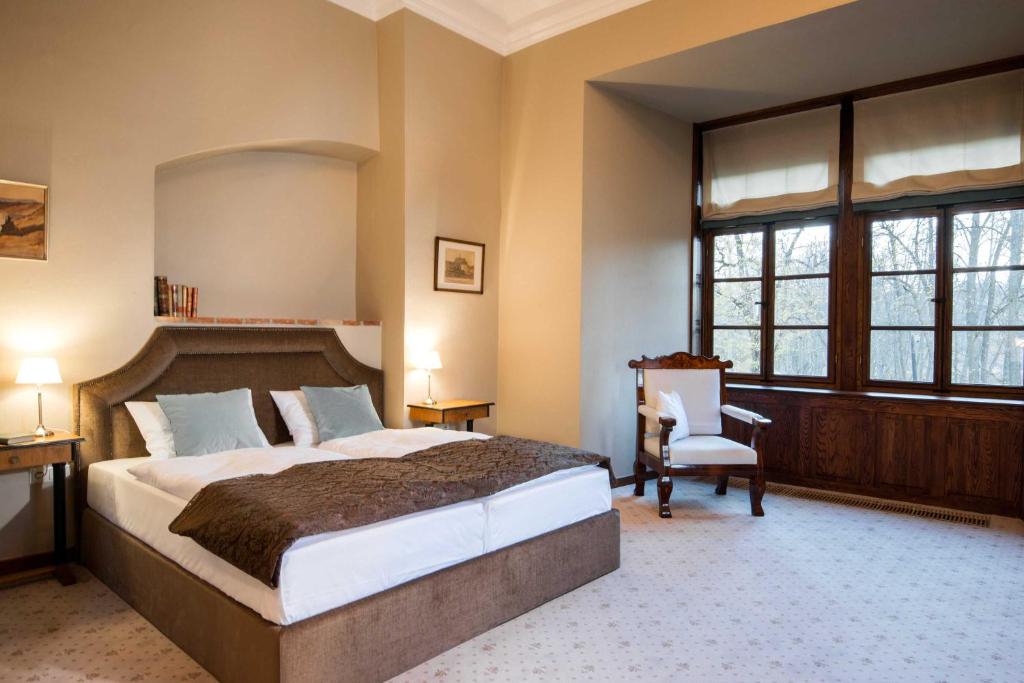 Spacious bedroom with king bed, upholstered headboard, bedside lamps, wooden-framed windows overlooking trees.