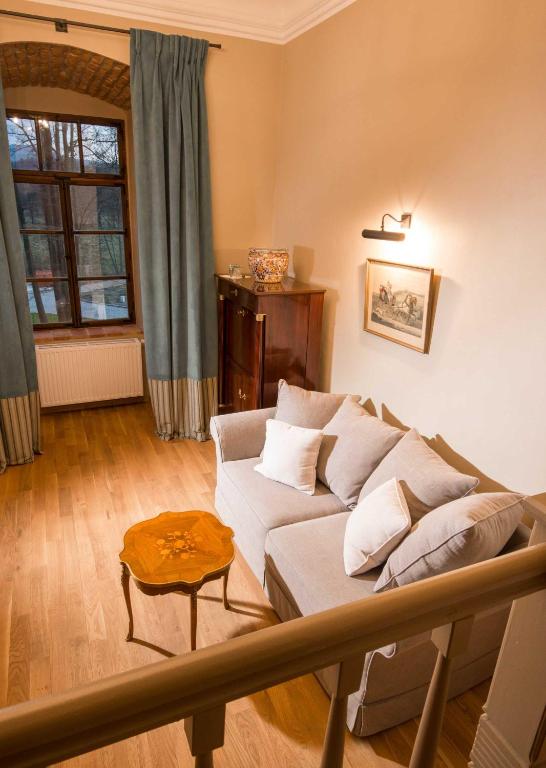 Cozy sitting nook with beige sofa, patterned wooden side table, tall green curtains, soft warm lighting.