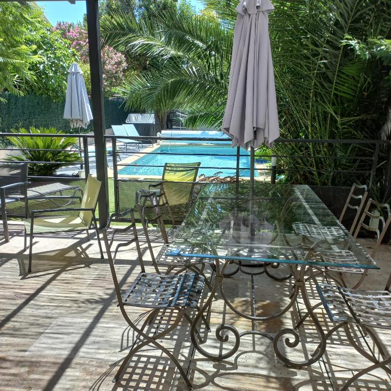 une table et des chaises en verre avec un parasol et une piscine dans l'établissement La Secrète d'Avignon, à Avignon