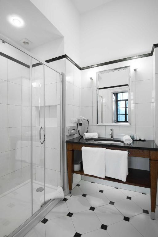 Contemporary bathroom with glass shower enclosure, black countertop vanity, white towels, geometric tiled floor, small window.
