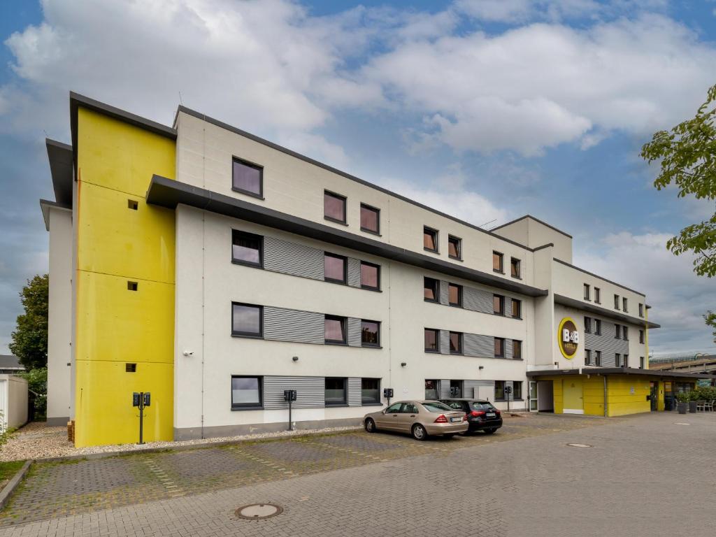 un bâtiment jaune et blanc avec une voiture garée devant dans l'établissement B&B Hotel Koblenz, à Coblence