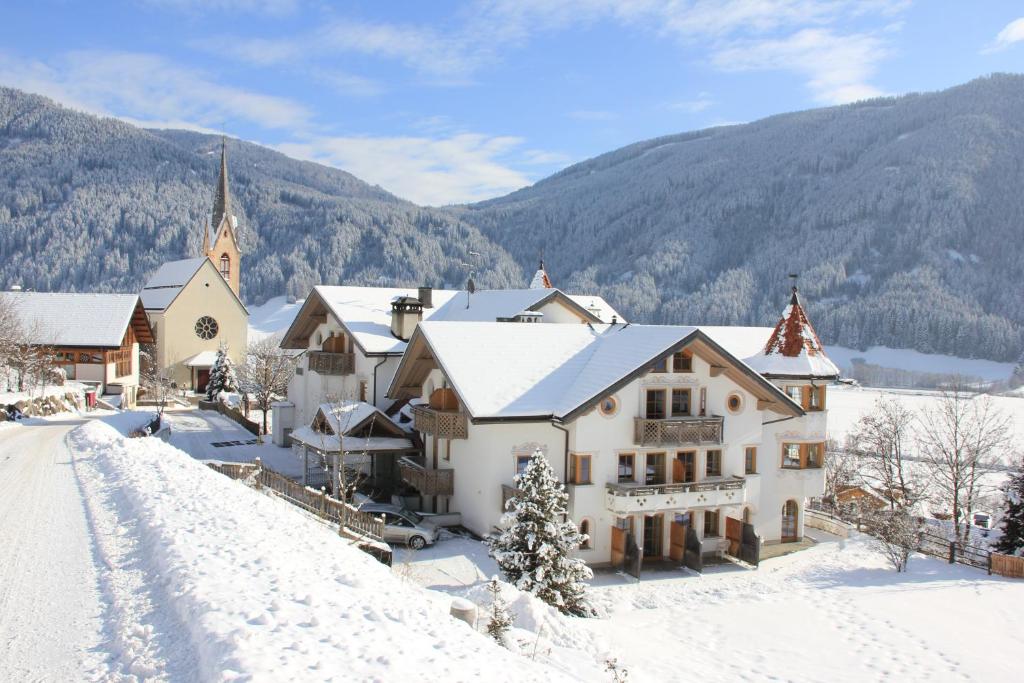 a house in the snow with a church at Turmhotel Gschwendt in Valle Di Casies
