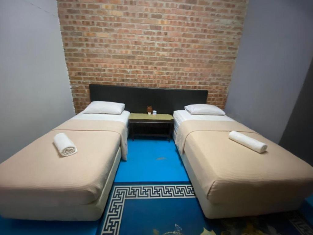 three beds in a room with a brick wall at Naja Hotel in Kampung Rahmat