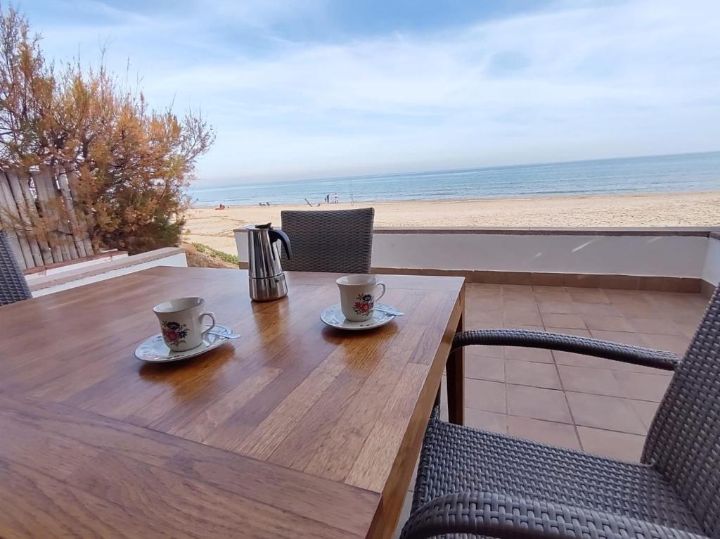 Apartament Tere في أوليفا: طاولة خشبية مع كوبين قهوة على الشاطئ