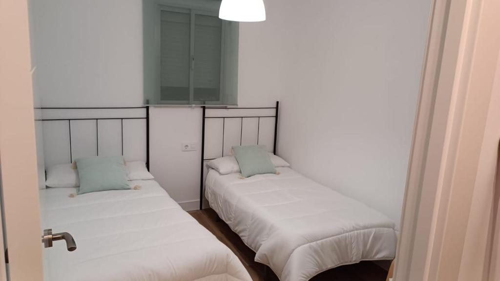Habitación con 2 camas, sábanas blancas y almohadas azules. en Piso cercano al recinto ferial, en Jerez de la Frontera