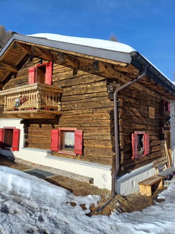 una baita di tronchi con finestre rosse con persiane nella neve di Chalet Shalom a Livigno