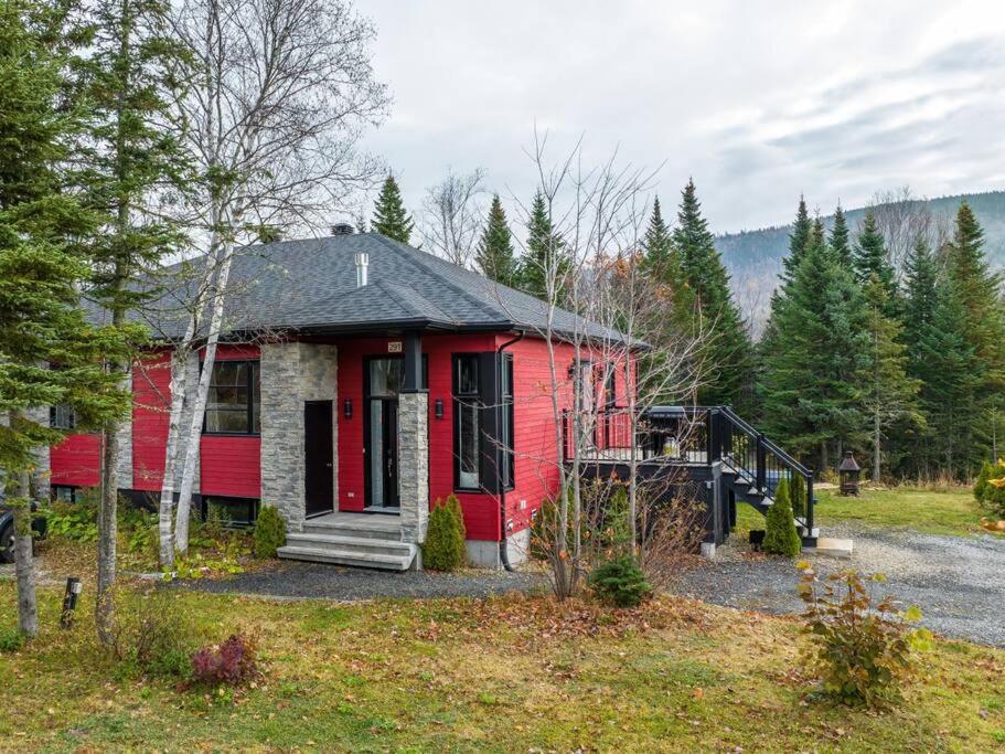 a red house in the middle of a field at Chalet des Érables-3 bedrooms, jacuzzi & relax in Petite-Rivière-Saint-François