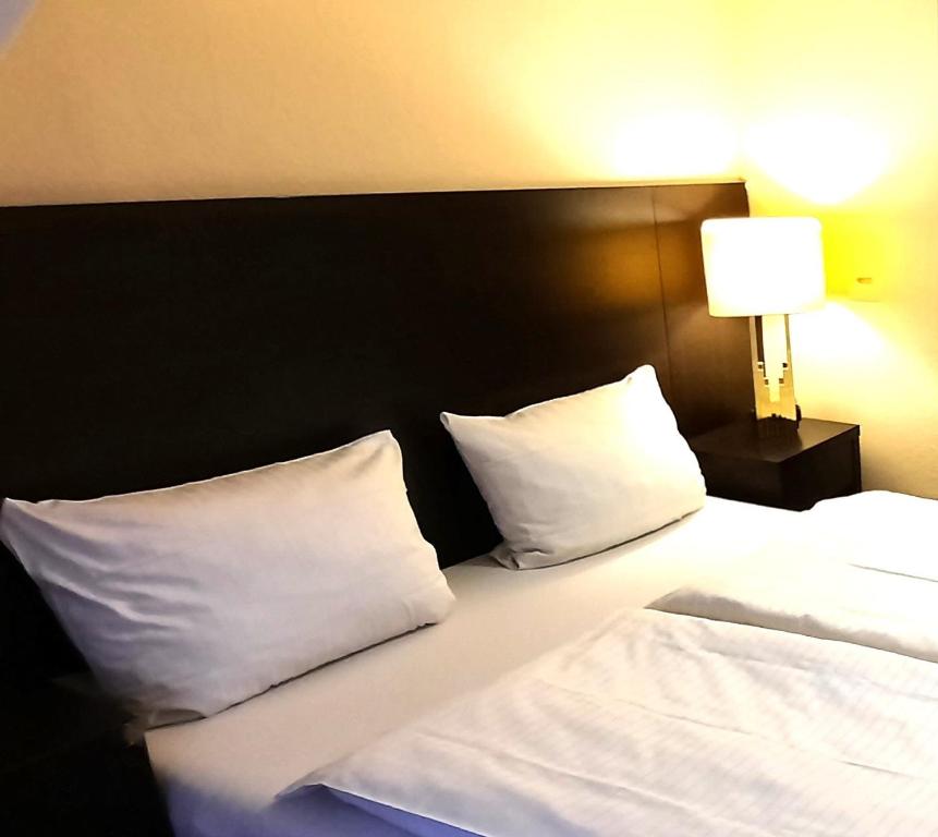 Bett mit weißen Kissen in einem Hotelzimmer in der Unterkunft Hotel Ariana in Köln