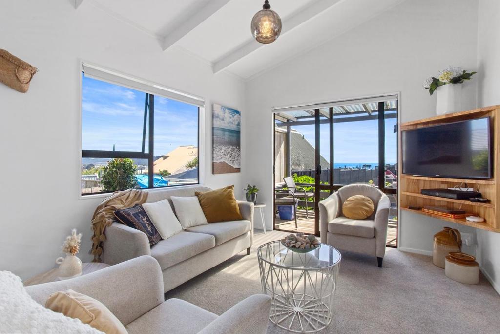 a living room with white furniture and large windows at Beverley Hills Guesthouse in Whangamata