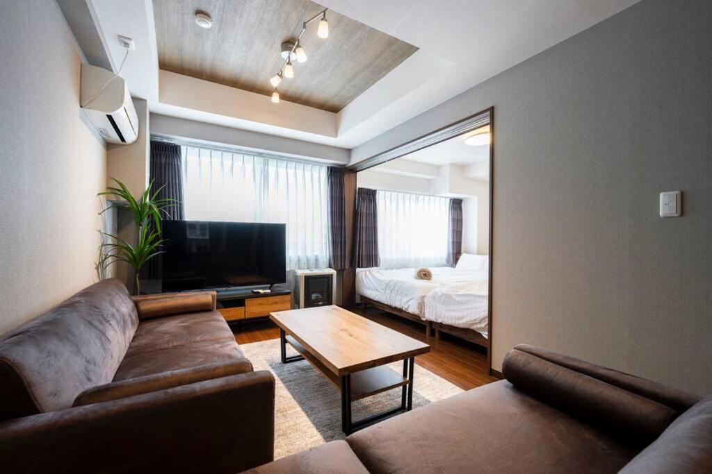 a living room with a couch and a tv and a bed at Shizuk+O Stay in Sapporo