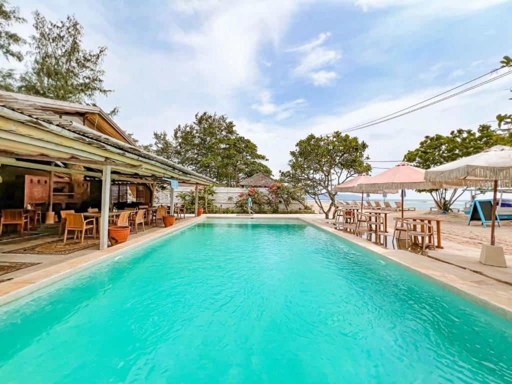 a swimming pool with tables and chairs next to a house at BUNGALOW CAFE GILI BEACH FRONT in Gili Meno