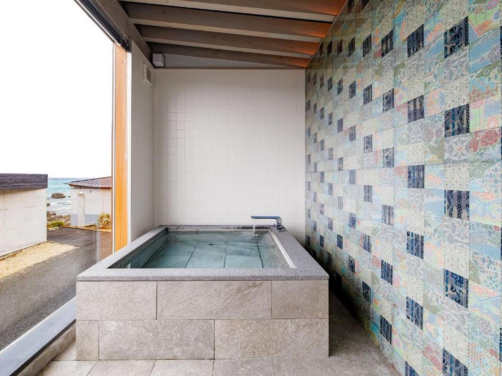 a bath tub in a room with a tile wall at Denpaku The Beachfront MIJORA in Amami
