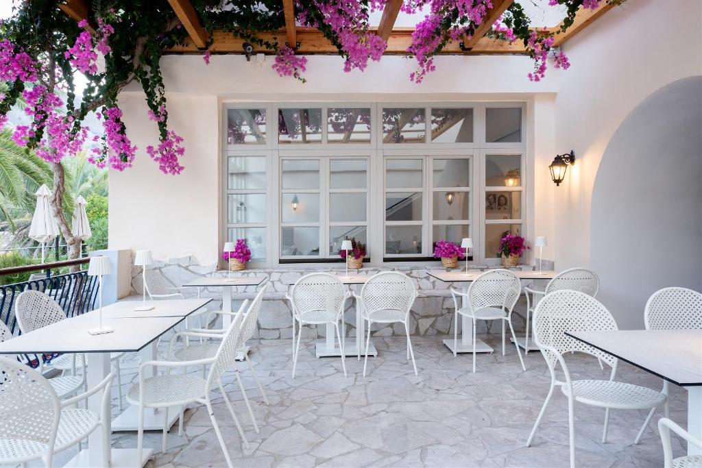 a restaurant with white tables and chairs and purple flowers at Pedi Beach Hotel in Symi