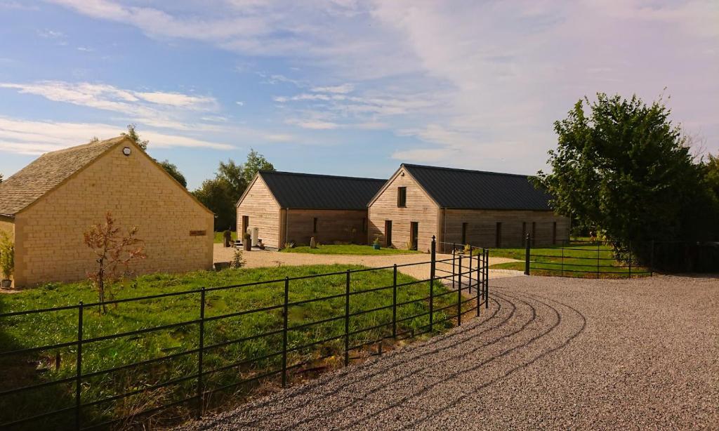 a group of three barns in a field with a fence at Luxury Lodge @ Ewen Barn - private 5* retreat in Cirencester