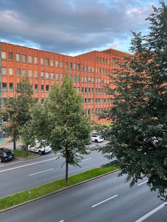un grand bâtiment en briques rouges avec des arbres en face d'une rue dans l'établissement Moderne und helle Ferienwohnung im Herzen der Stadt, à Dortmund