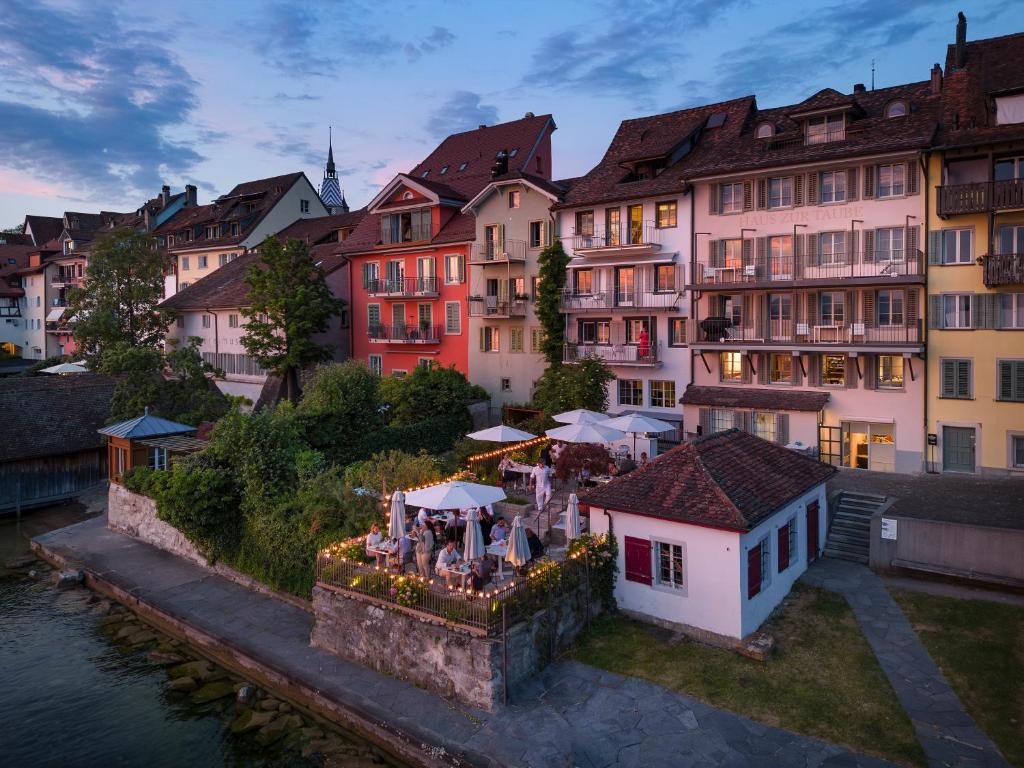 a group of people standing near a building next to a river at La Colombe Boutique Hotel in Zug