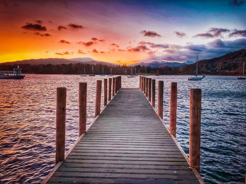 a wooden pier in the water with a sunset at Stylish, family friendly central Windermere home with wood burner in Windermere