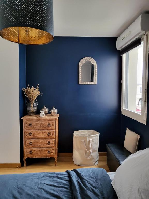- une chambre avec des murs bleus, un lit et une table de chevet dans l'établissement Appartement en Location pour les Jeux Olympiques, à Deuil-la-Barre