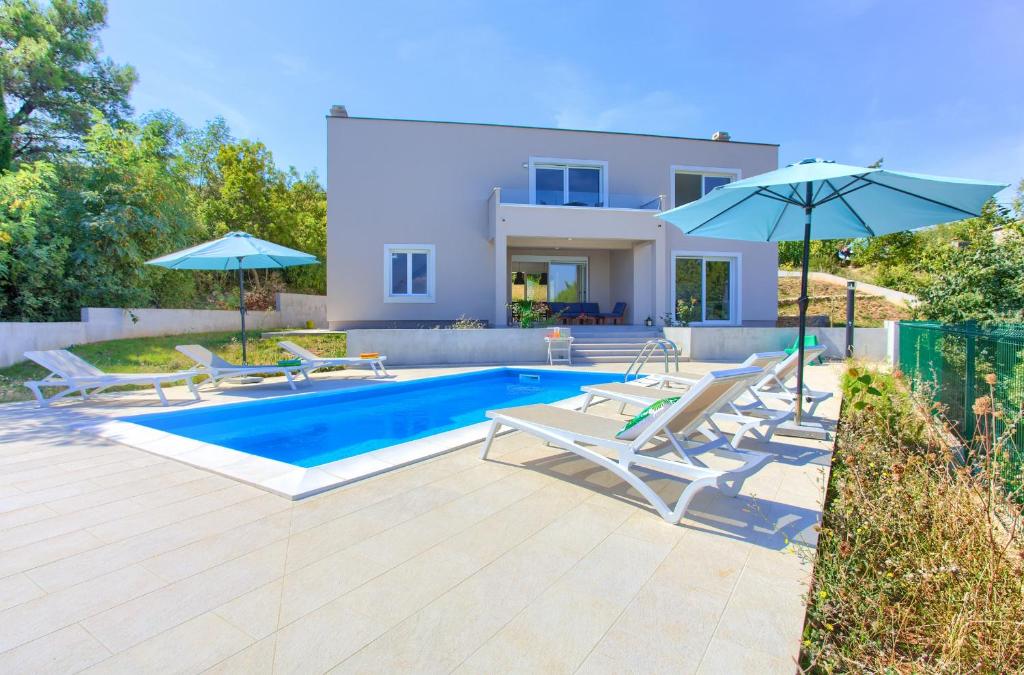 a swimming pool with chairs and umbrellas in front of a house at Villa Olivia in Vrh