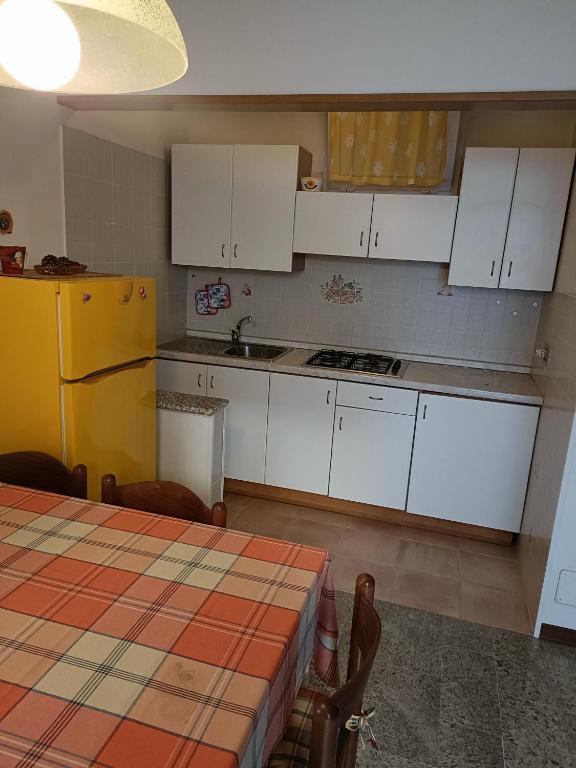 La cuisine est équipée de placards blancs, d'une table et d'un réfrigérateur jaune. dans l'établissement Casa Diana, à Bibione