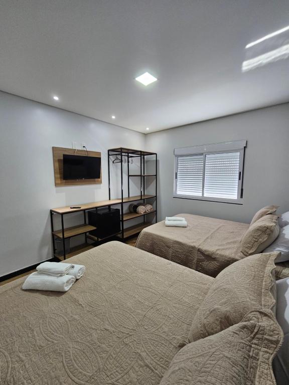 a bedroom with two beds and a desk and a television at POUSADA CITRINO in Ametista do Sul