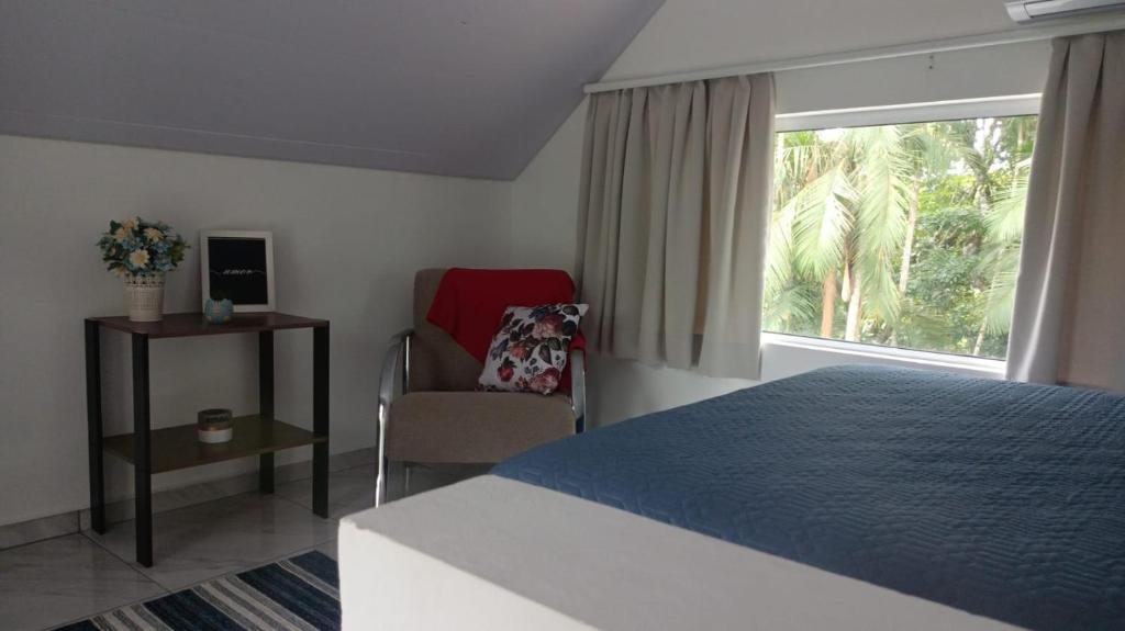 um quarto com uma cama, uma cadeira e uma janela em Chalé Lua Azul em Jaraguá do Sul