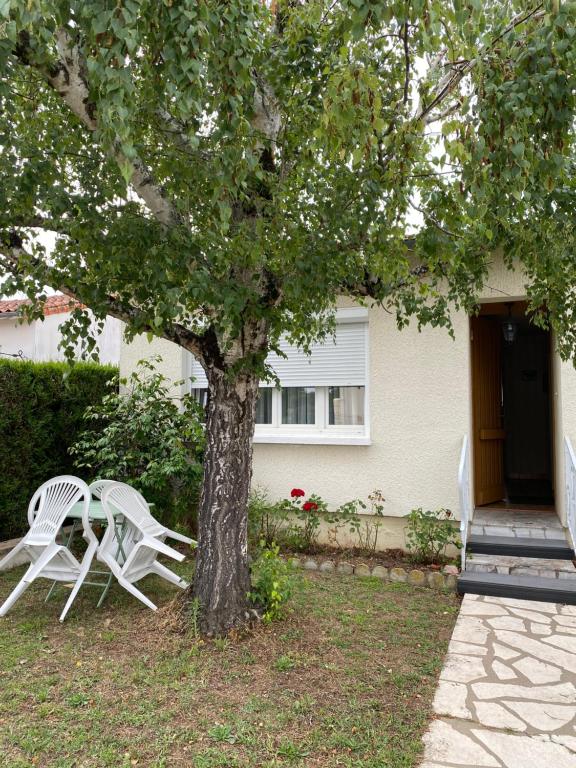 2 chaises blanches assises à côté d'un arbre devant une maison dans l'établissement Maison de famille proche Futuroscope, à Châtellerault