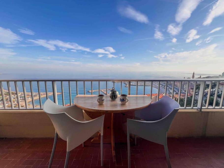 un tavolo e sedie su un balcone con vista sulla spiaggia di Menton - Vue panoramique exceptionnelle ! 4Pers a Mentone