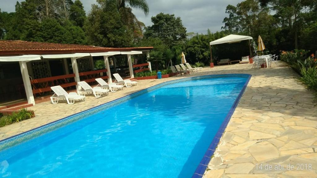 a blue swimming pool with chairs and a house at Hotel Araucaria Cotia in Vargem Grande Paulista