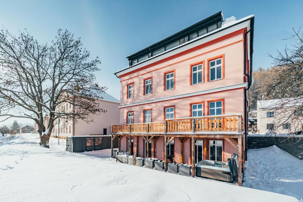 un bâtiment rose avec un balcon dans la neige dans l'établissement Apartmán Horský Sklípek, à Žacléř